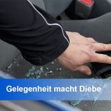 Hand greift durch ein eingeschlagenes Autofenster zu einem schwarzen Portemonnaie